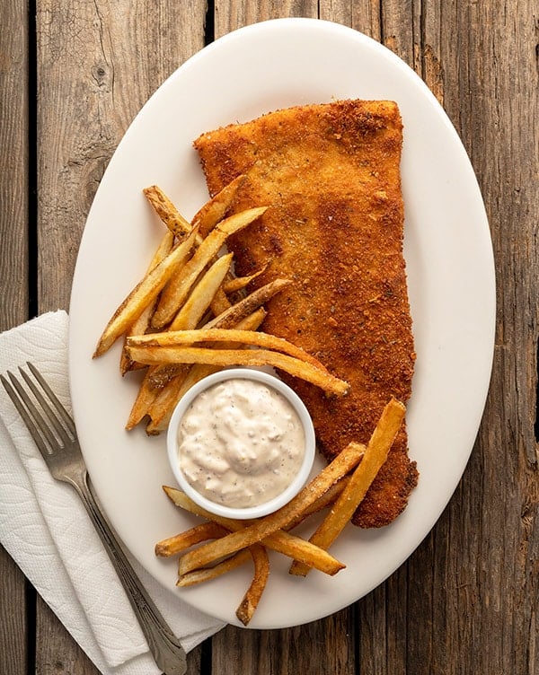 fried flounder with tartar sauce and homemade fries on the plate.