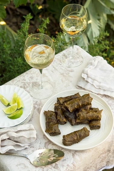 Grape leaf tamales on a plate with some white wine and limes.