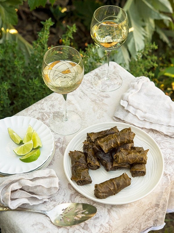 Grape leaf tamales on a plate with some white wine and limes. 