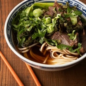 Close up of a bowl of Taiwanese beef noodle soup showing the herbs and bok choy.