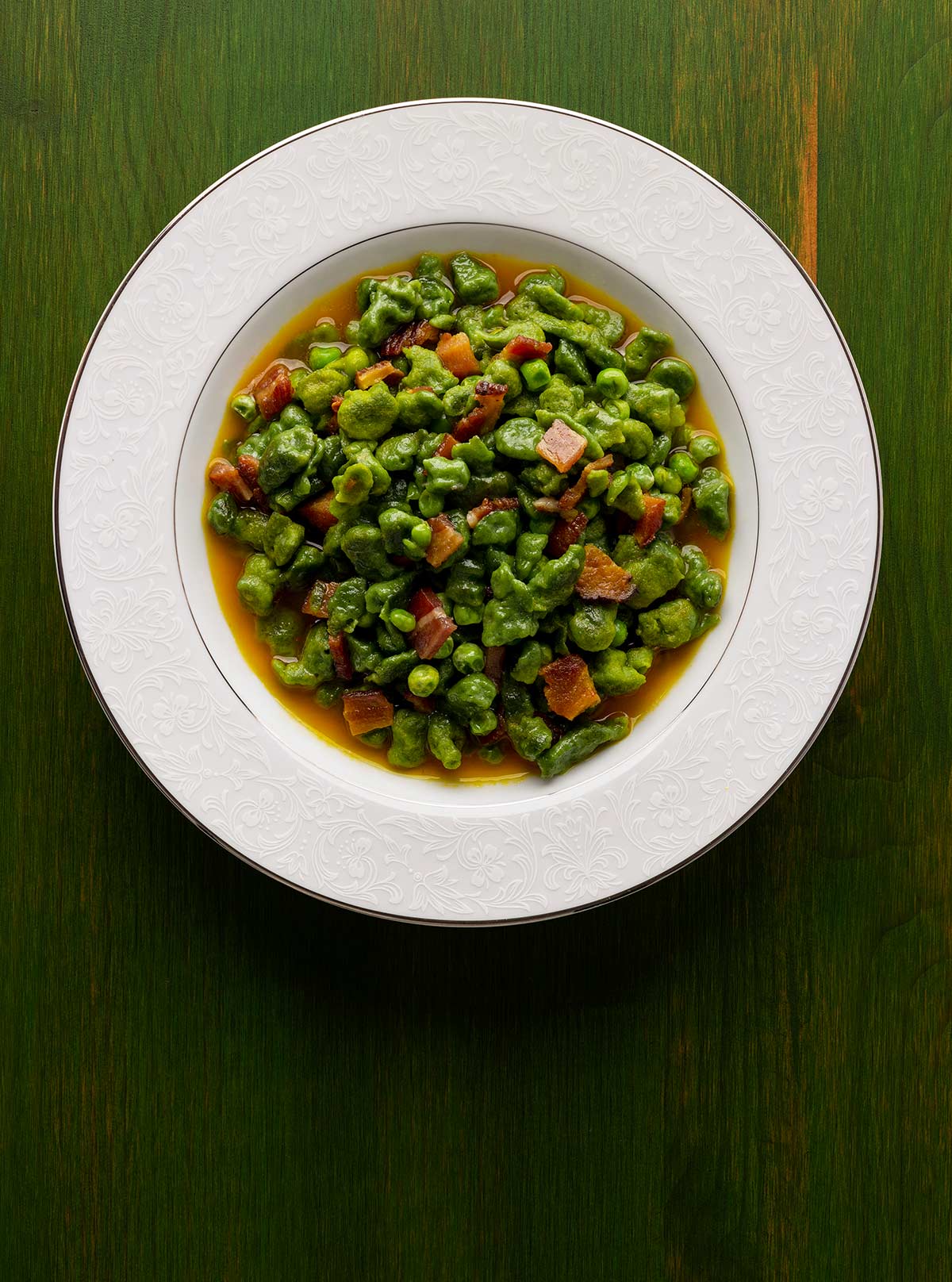 A bowl of spinach spaetzle with peas and bacon.