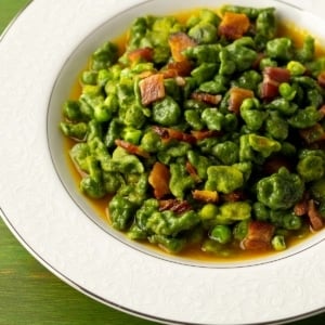 Closeup of a bowl of spinach spaetzle with peas and bacon.