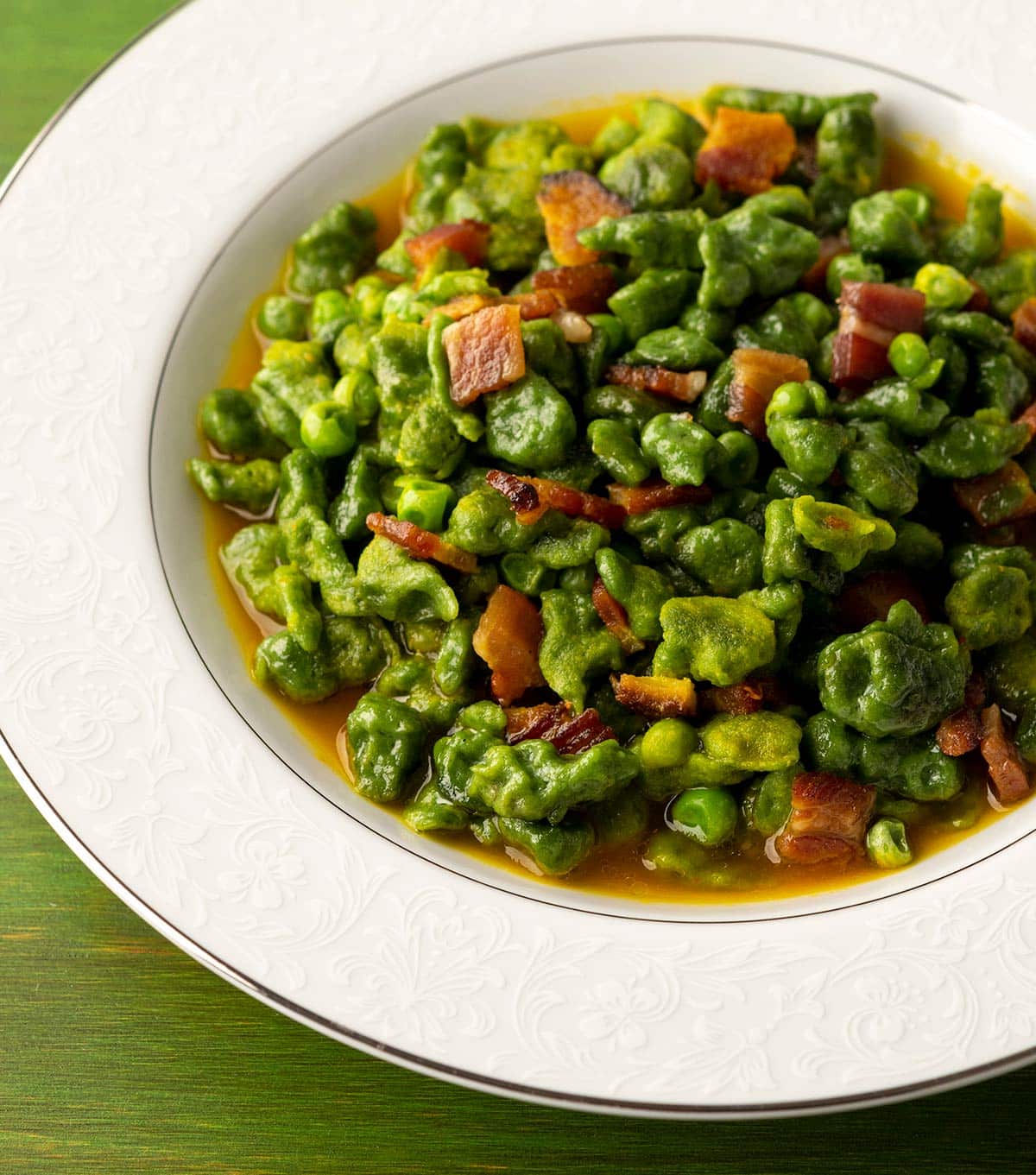 Closeup of a bowl of spinach spaetzle with peas and bacon. 