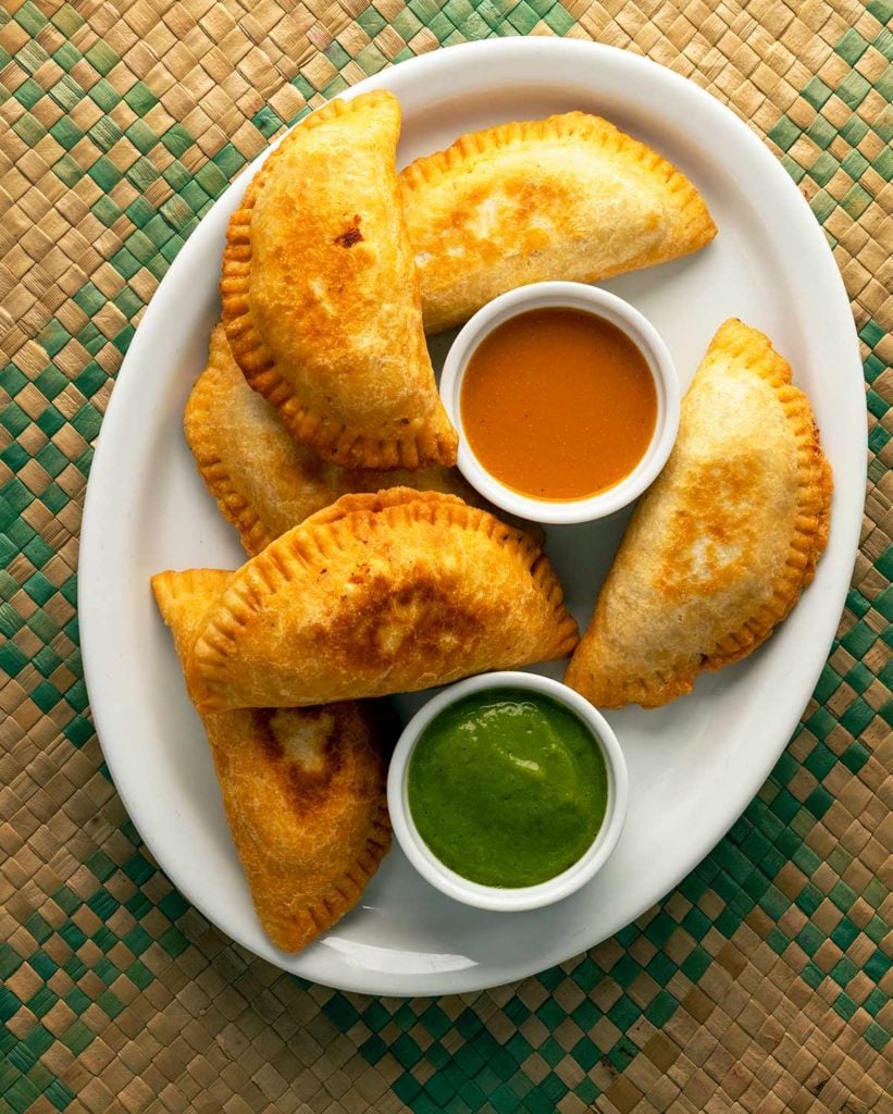 A platter of fried empanadas with salsa. 