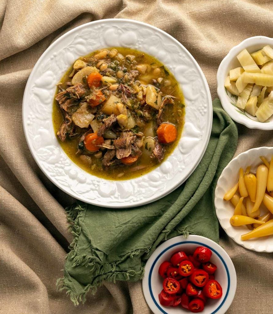 A bowl of duck stew with pickled vegetables alongside. 