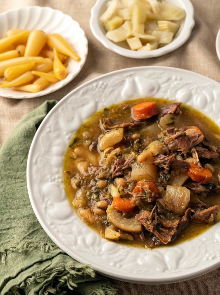 Closeup of a bowl of duck stew with accompanying pickles.