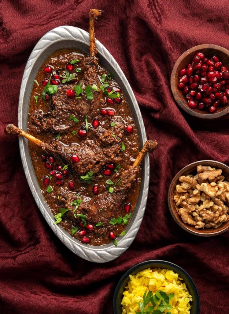 A platter of fesenjan with bowls of walnuts, pomegranate and rice. 