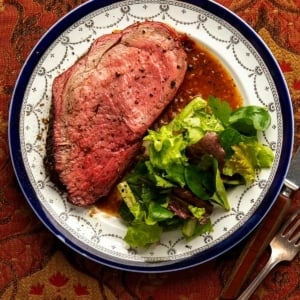 A slice of elk roast on a plate with a salad.