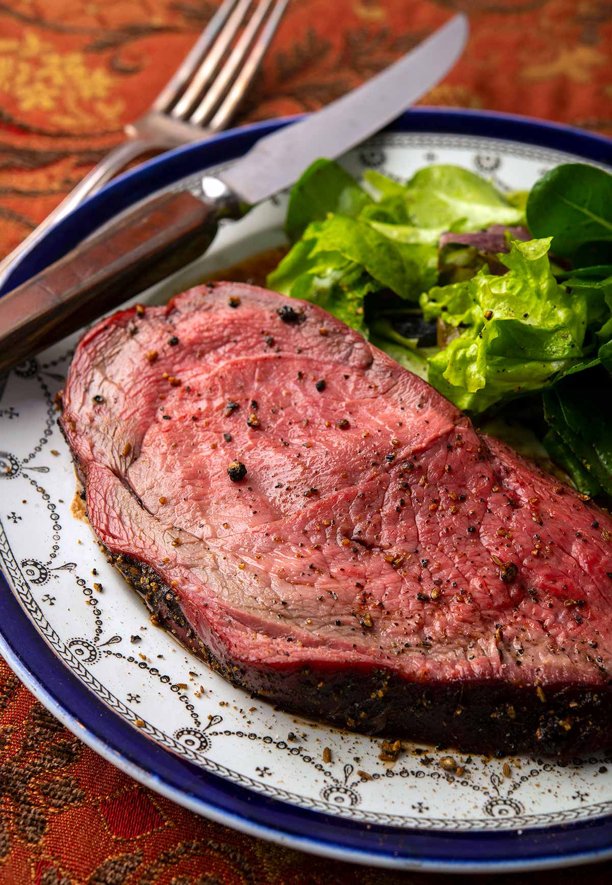 A thick slice of elk roast with a salad on a plate. 