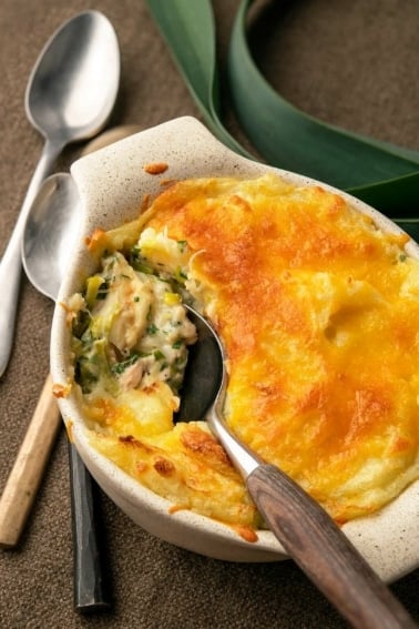 Fish pie with leeks being spooned out of a casserole.