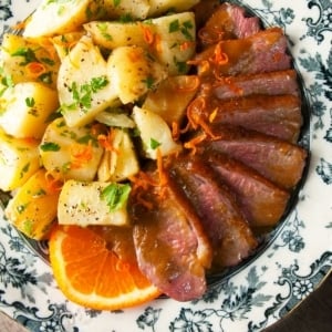 Duck with bigarade sauce and potatoes on a plate.