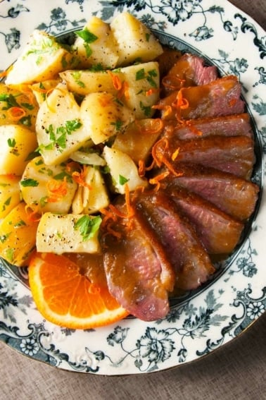 Duck with bigarade sauce and potatoes on a plate.