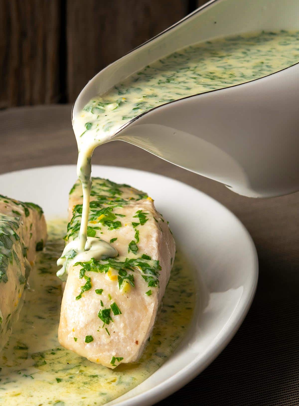 Pouring parsley sauce from a gravy boat onto fish. 