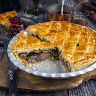 A British duck pie on a platter with a piece removed.