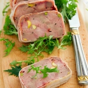 Slices of duck terrine on a cutting board with leaves of frisee.