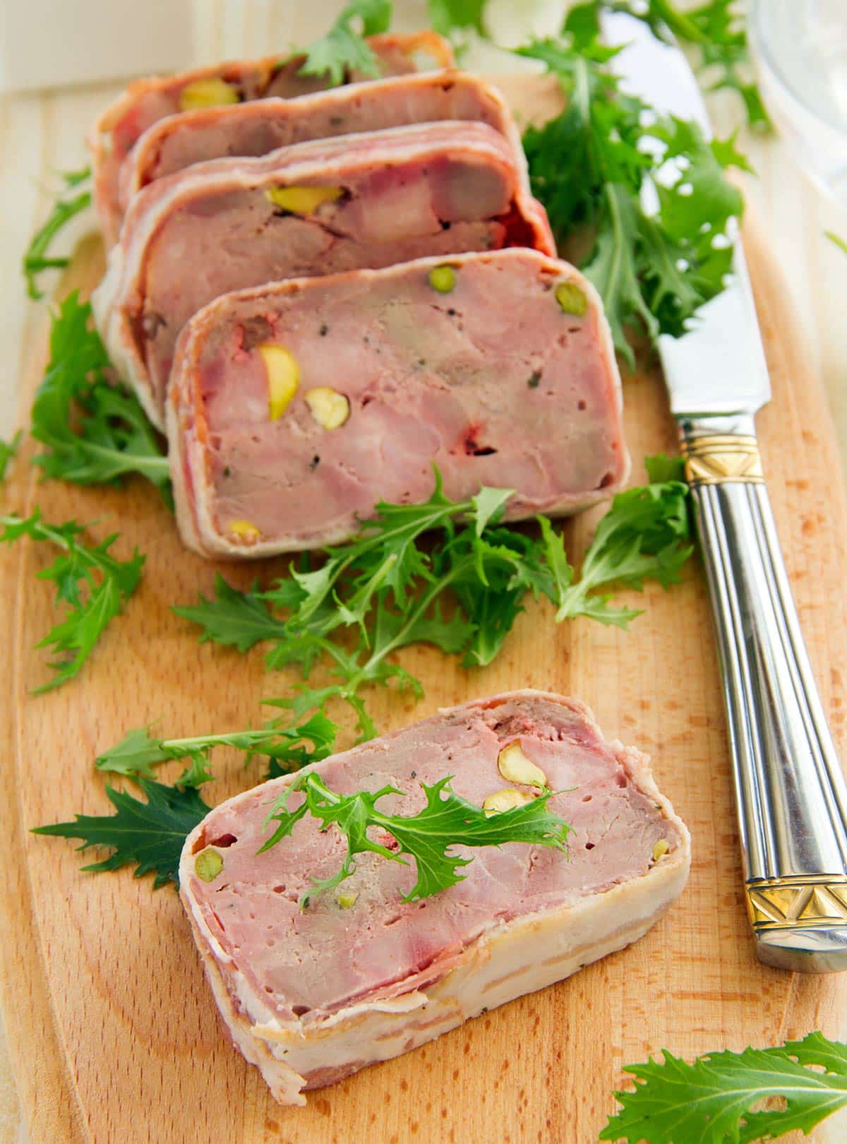 Slices of duck terrine on a cutting board with leaves of frisee. 