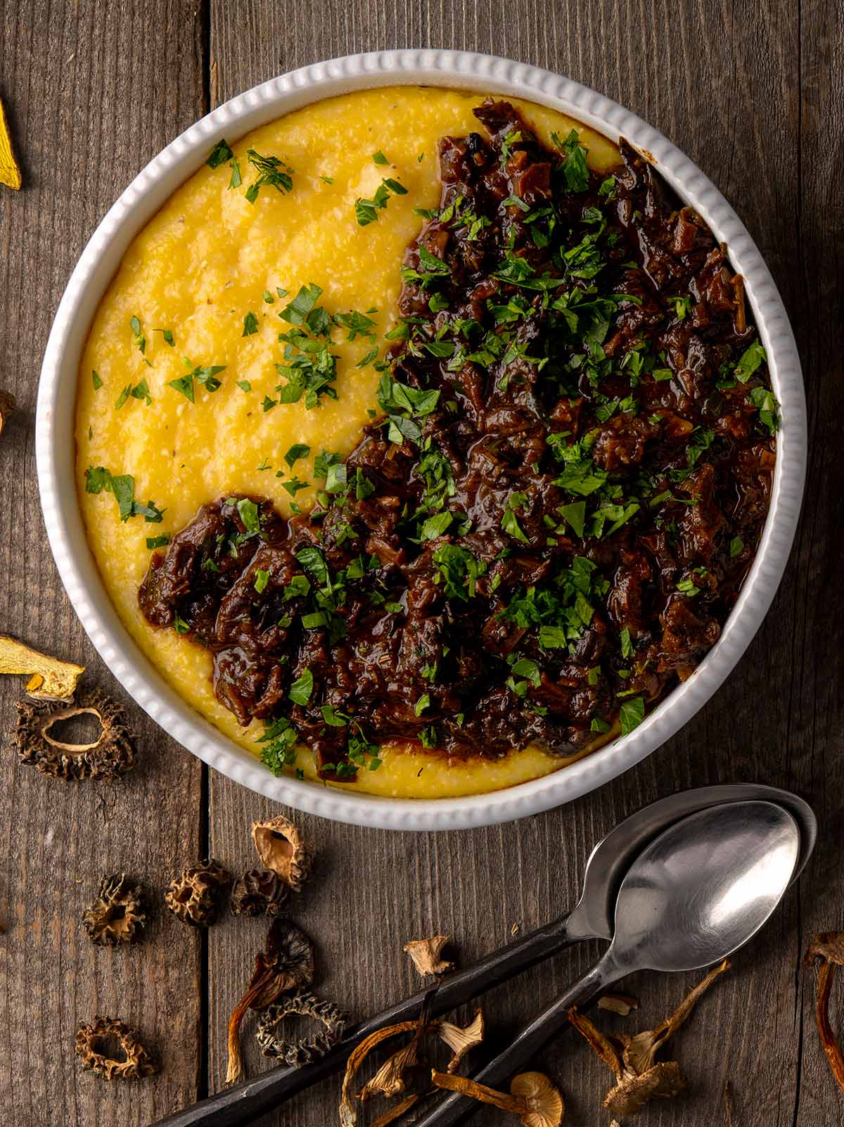 A bowl of polenta with mushroom ragu, with dried mushrooms alongside. 