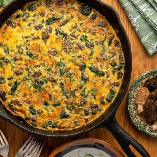 Close up of mushroom spinach frittata in a cast iron pan on a table.