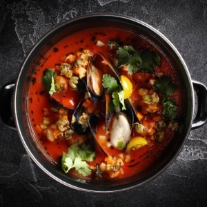 A bowl of mussel soup with tomato.