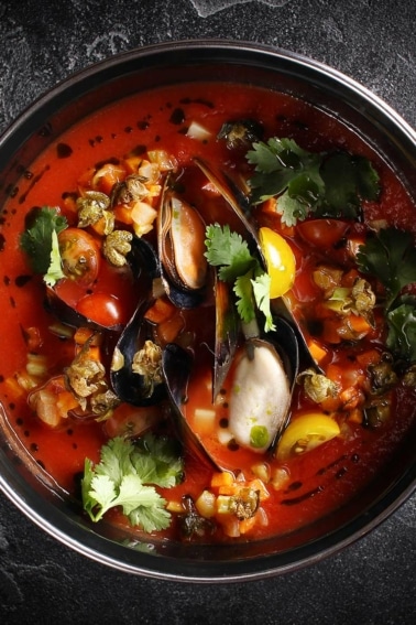 A bowl of mussel soup with tomato.