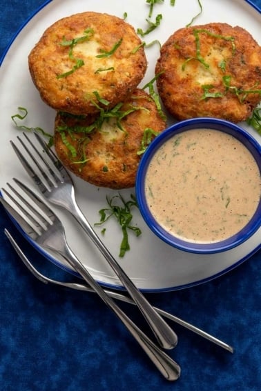 Three potato fish cakes on a plate with remoulade sauce.