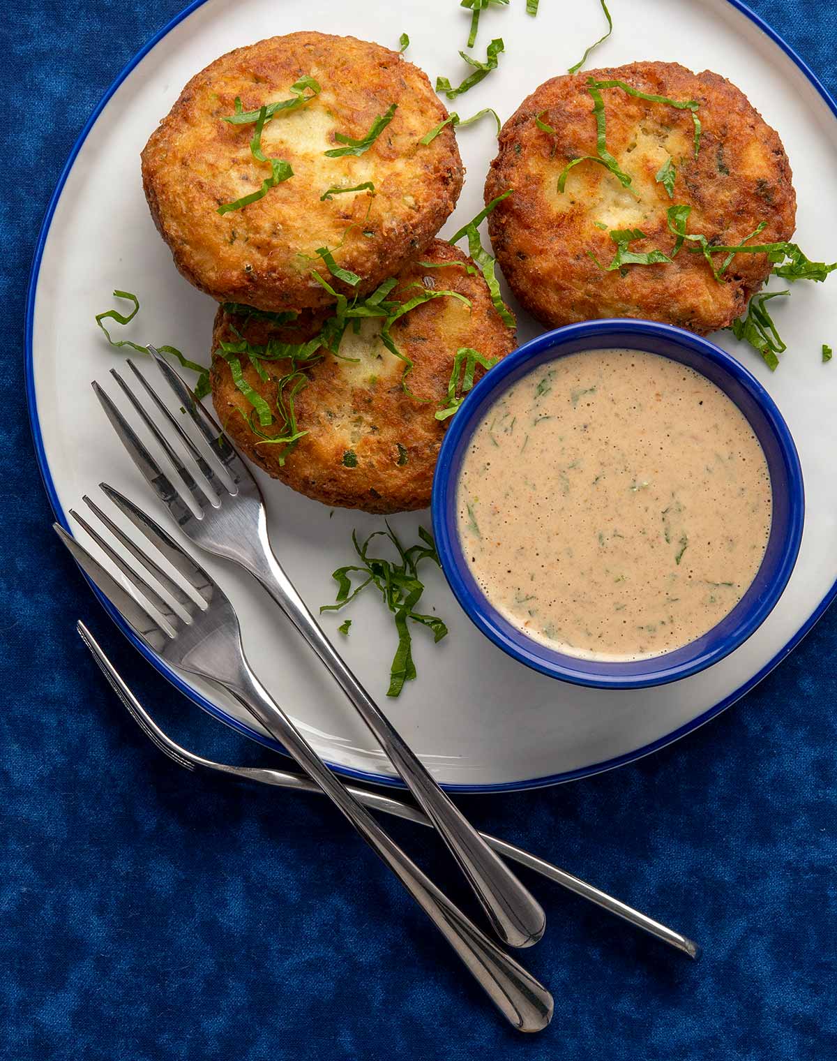 Three potato fish cakes on a plate with remoulade sauce.