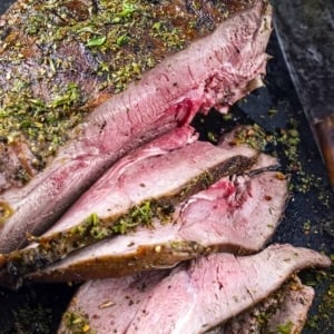 Roast haunch of venison with herbs on a cutting board.