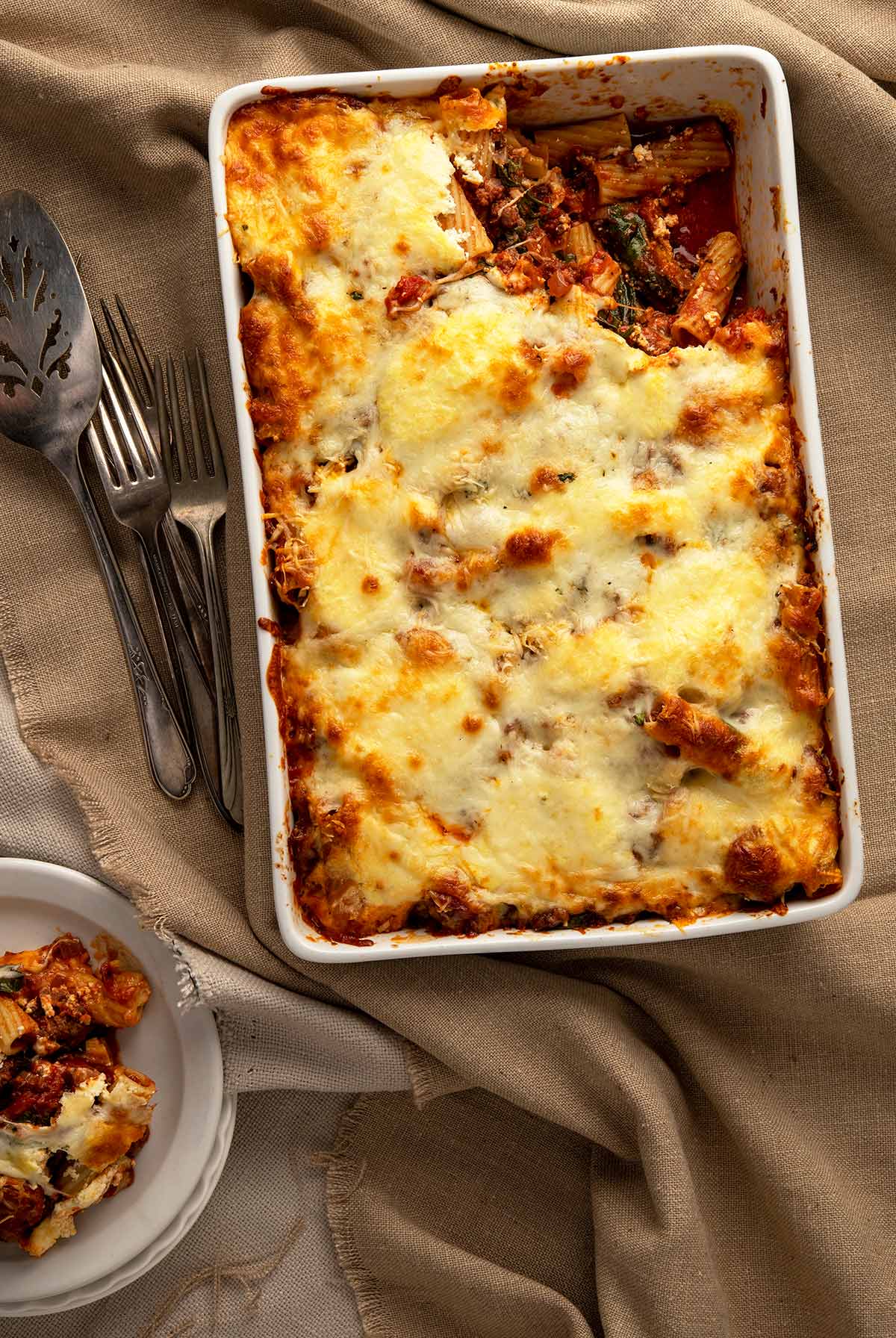 A venison casserole in the style of baked ziti, on a table with a portion dished out. 