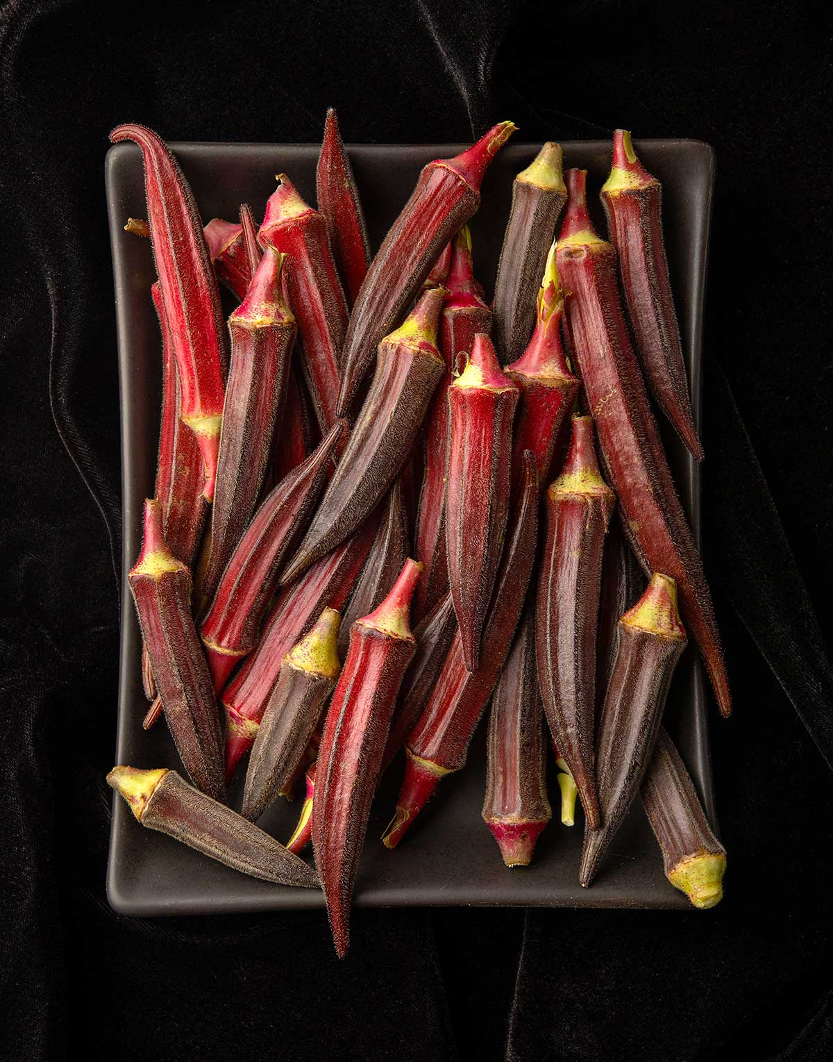 Yuma red okra on a small plate on a black velvet background. 