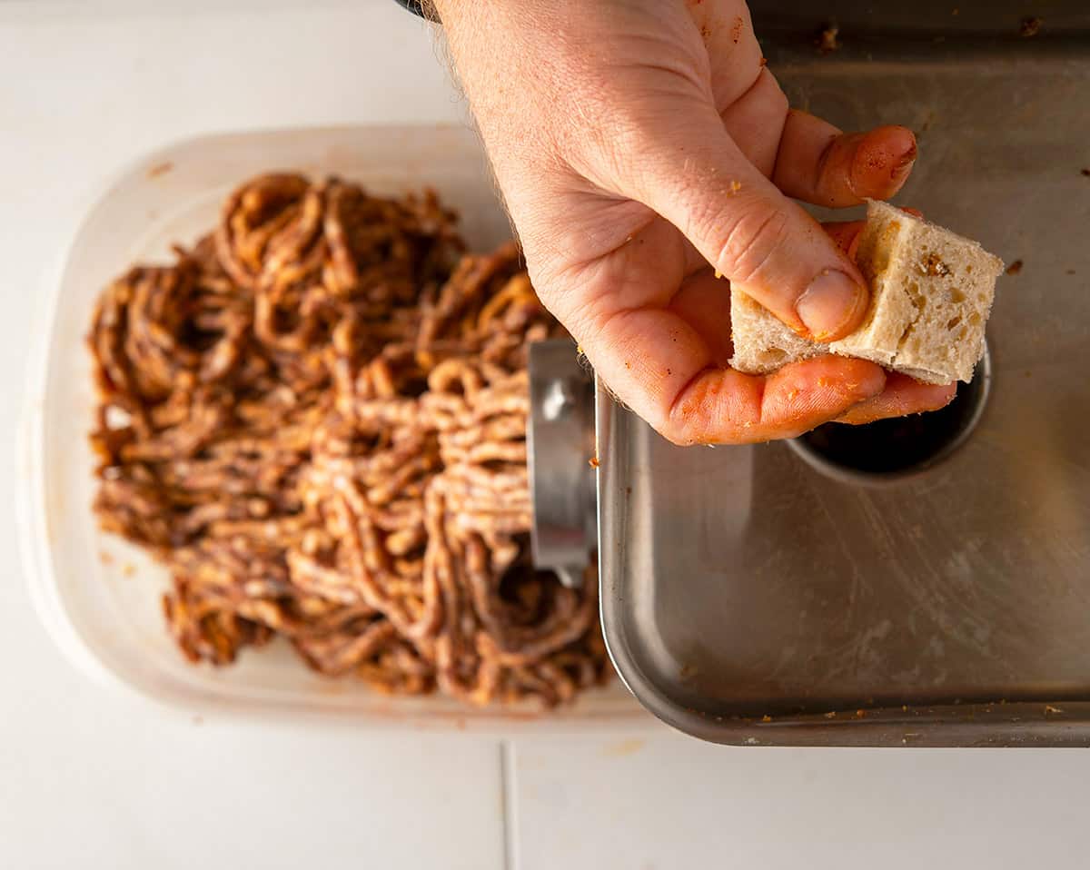 Dropping bread cubes into the grinder to push out every bit of meat left in it. 