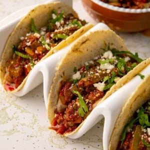 Close up of three tacos filled with carne con nopales on a taco holder.