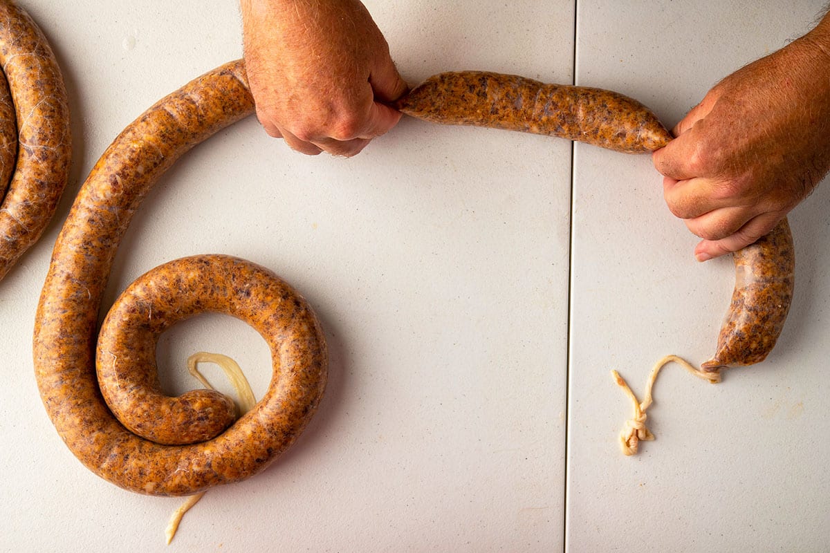 Pinching off a link of homemade sausage from the coil.