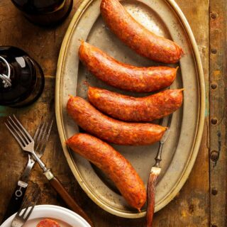 A platter of Texas hot links sausage on a table, with sliced links and potatoes.