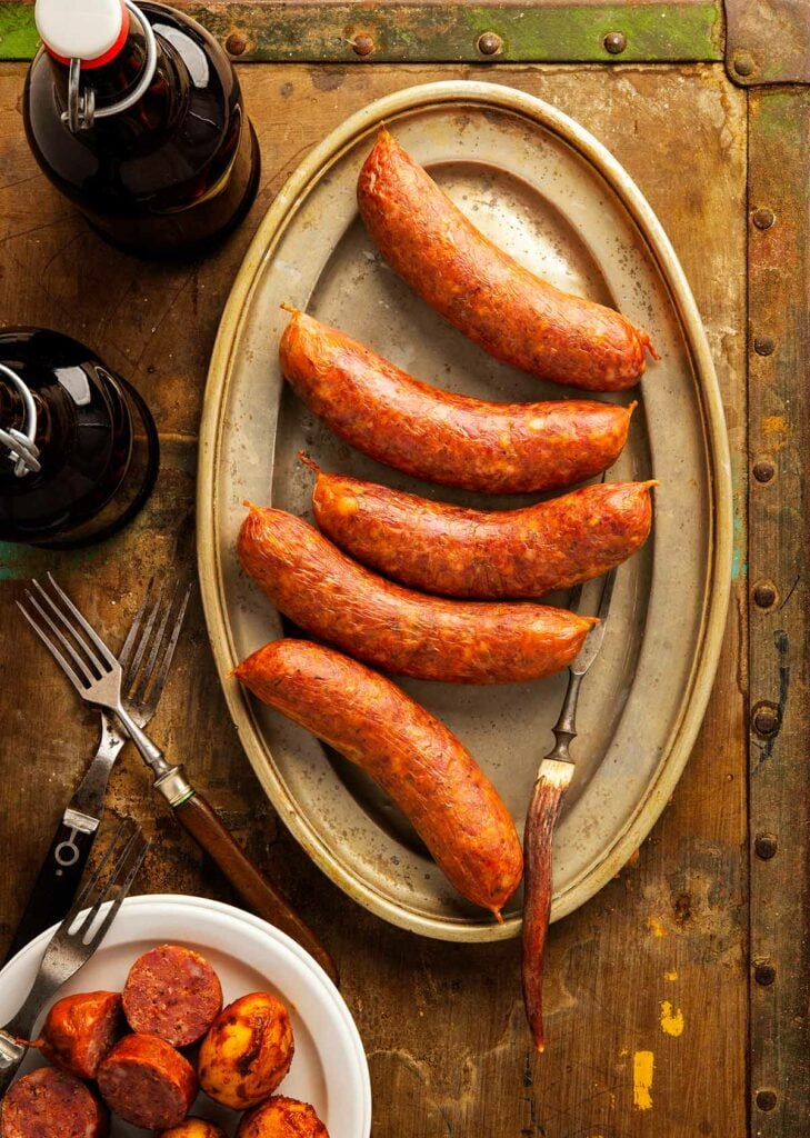 A platter of Texas hot links sausage on a table, with sliced links and potatoes.