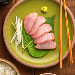 Hamachi sashimi on a plate with shiso, wasabi and julienned daikon radish.