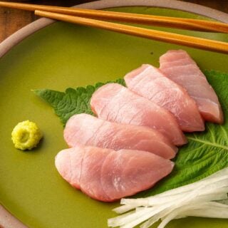 Slices of hamachi sashimi on a plate with daikon and shiso.