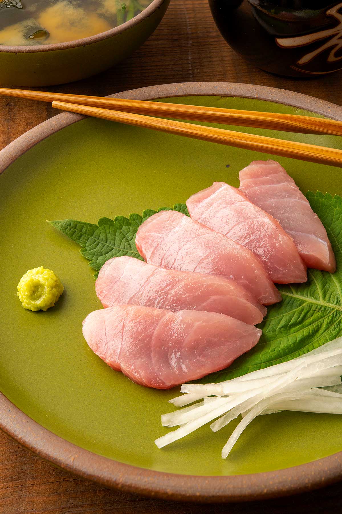 Close up of hamachi sashimi on a plate with daikon radish, wasabi and shiso.