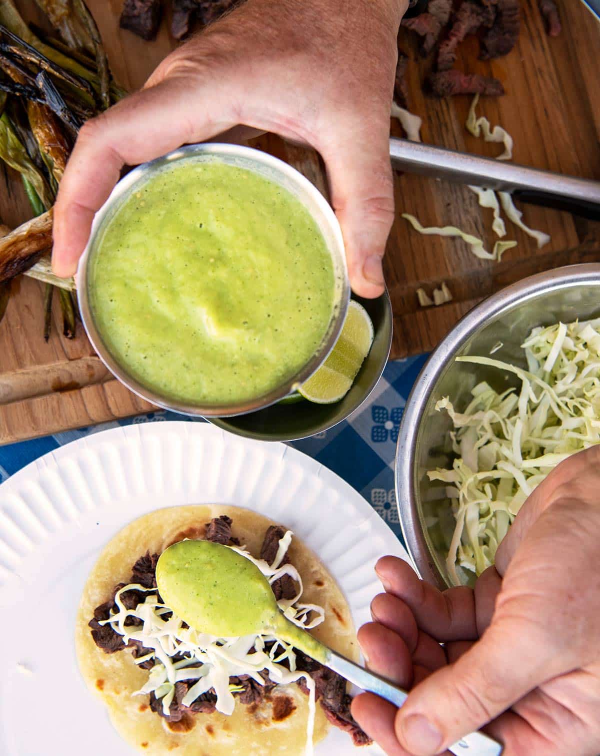 Spooning thin avocado salsa on tacos al carbon.