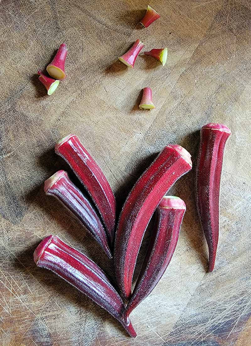 Red okra on a cutting board, with the stems removed. 