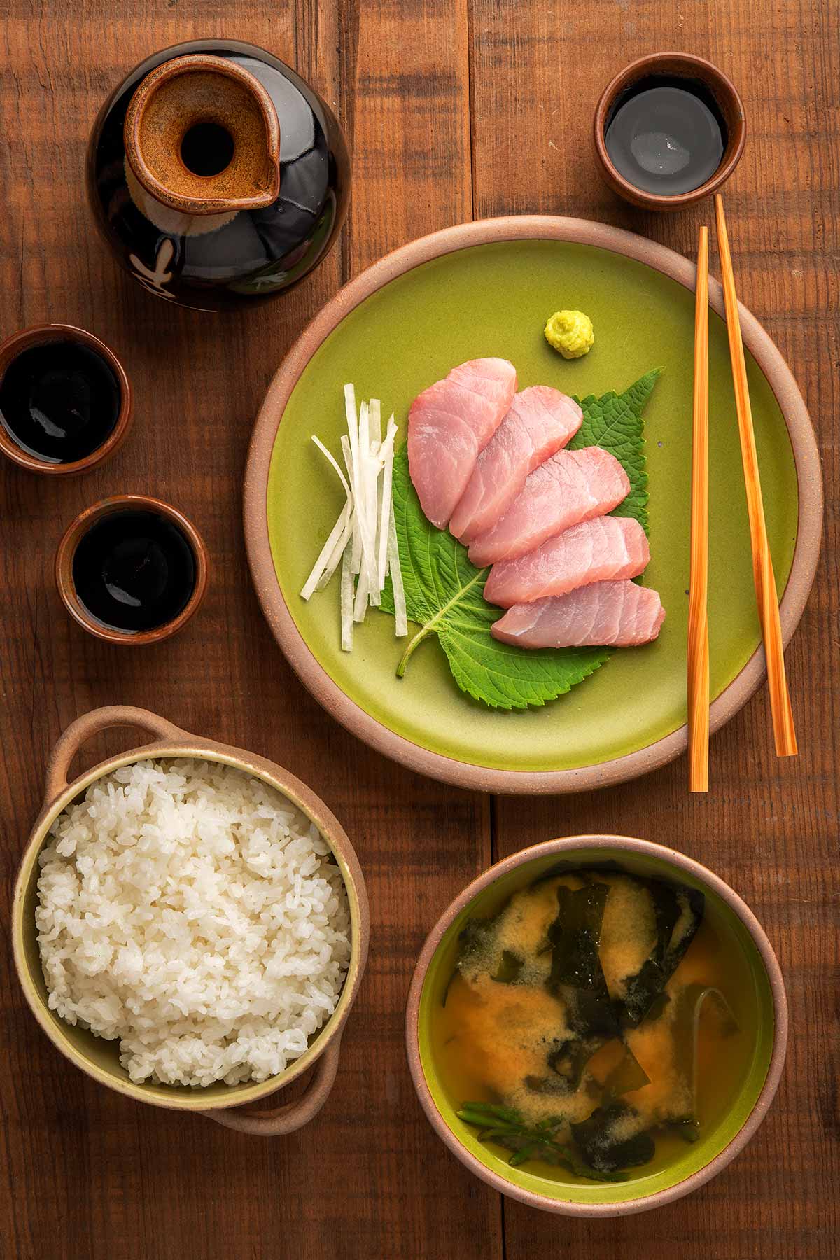 Yellowtail sashimi with rice, miso soup and sake, arranged on a table. 