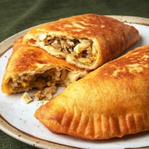 Two lihapiirakka, Finnish meat pies, on a plate with one broken open.