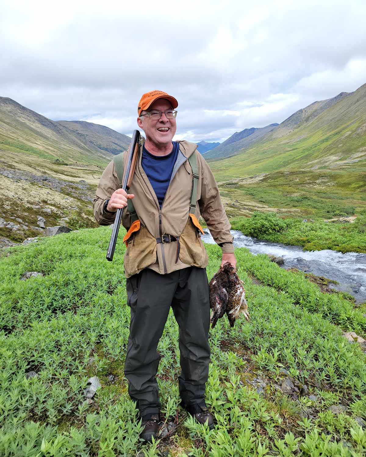 Hank Shaw holding two willow ptarmigan in an alpine valley in Alaska. 