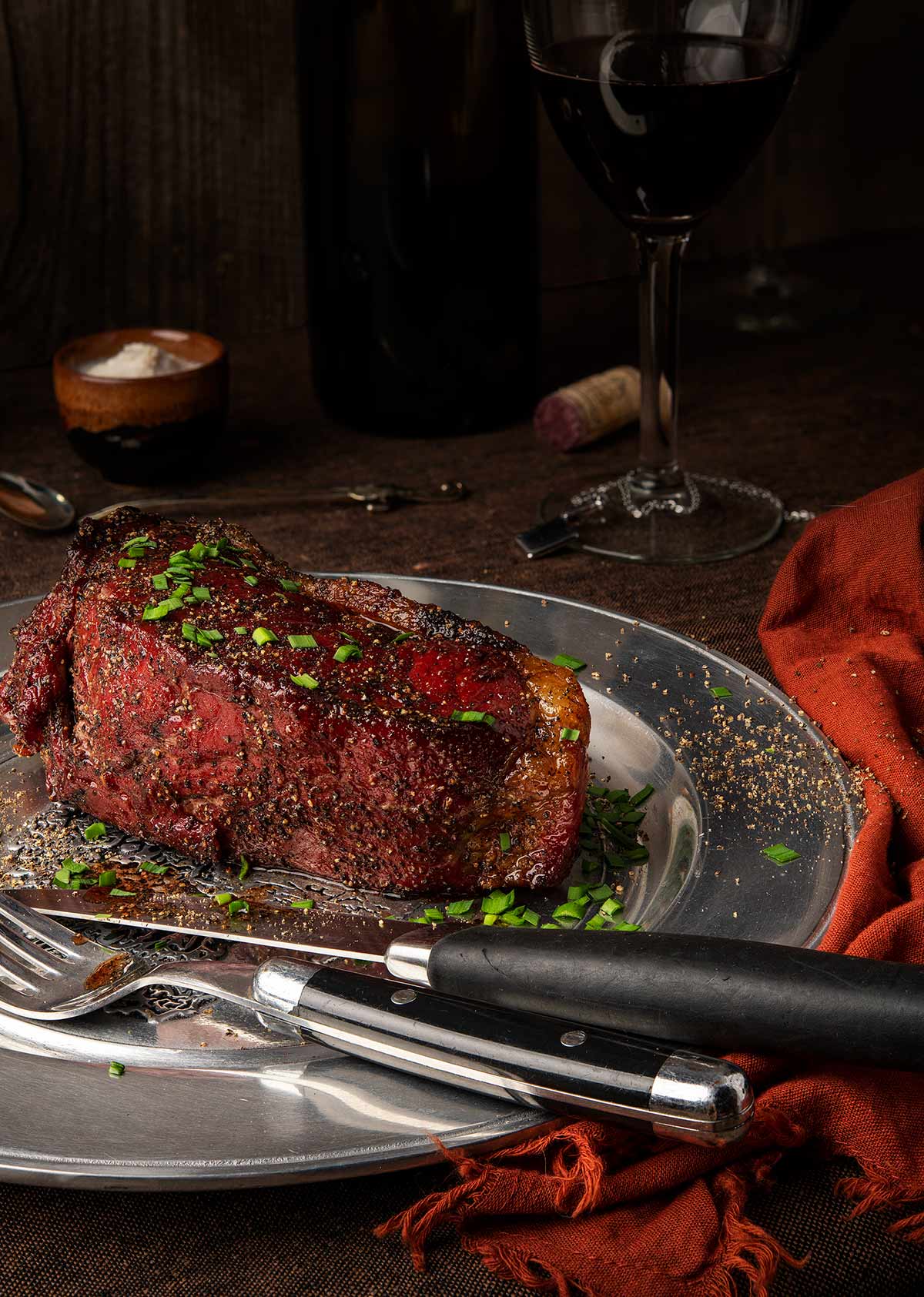 A bison steak on a plate with black pepper and chives. 