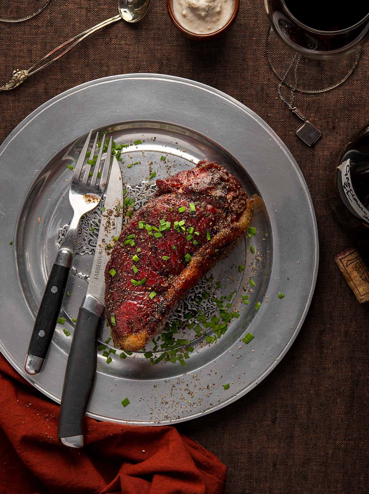 Overhead view of a seared bison steak on a plate with wine. 