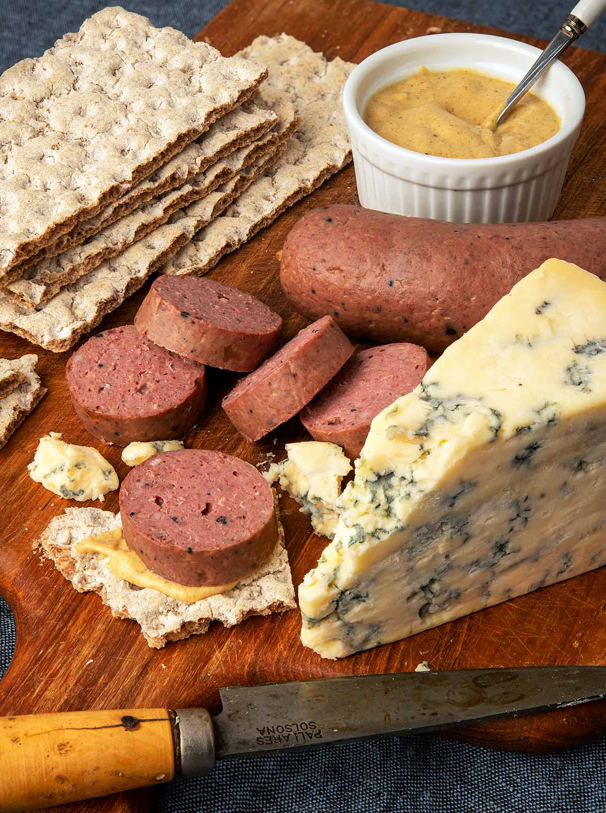 Slices of braunschweiger sausage with crackers, mustard and blue cheese. 