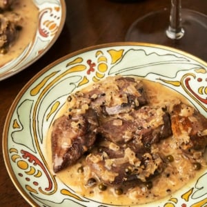 Dove breasts au poivre on a plate with a glass of wine.