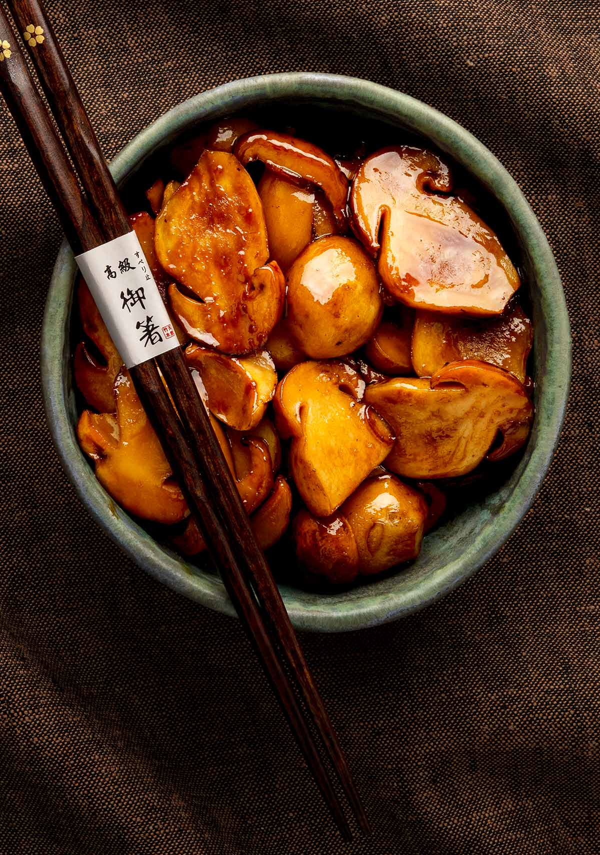A bowl of teriyaki mushrooms with a pair of chopsticks. 