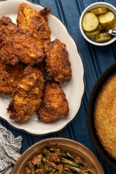 A platter of fried pheasant with pickles, cornbread and green beans.