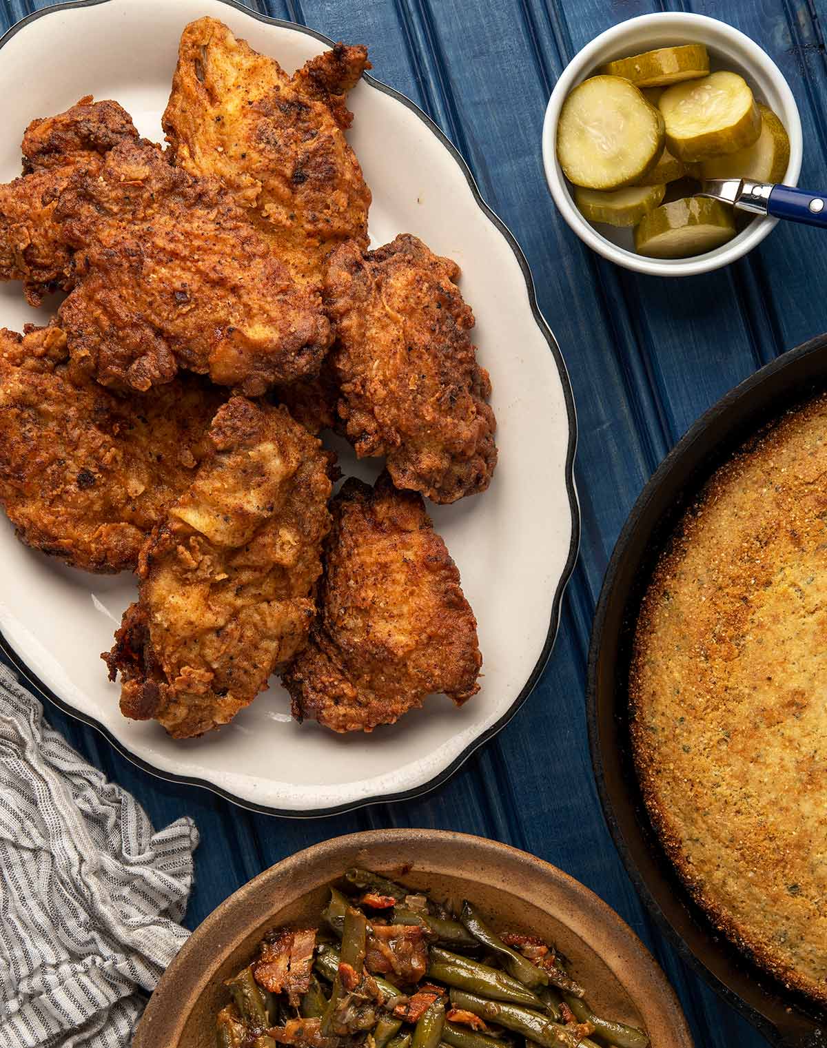 A platter of fried pheasant with pickles, cornbread and green beans. 