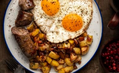 A plate with Swedish sausage, fried potatoes and sunny side up eggs.